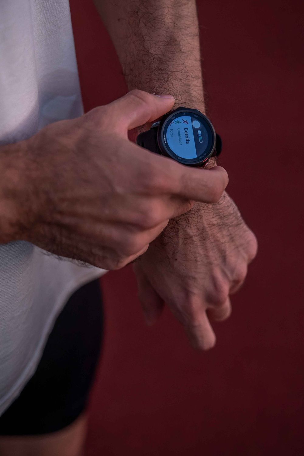 Primer plano de un corredor manejando un reloj deportivo en su muñeca junto a una pista de atletismo.