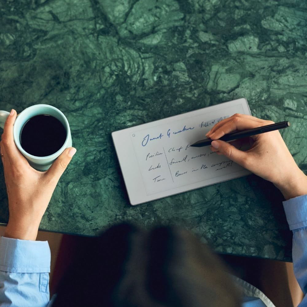 Persona escribiendo en una tablet reMarkable con un lápiz digital mientras sostiene una taza de café.