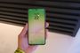 Samsung Galaxy A56 sostenido en una mano, con la pantalla de bloqueo encendida y un fondo en tonos verdes y rosas.