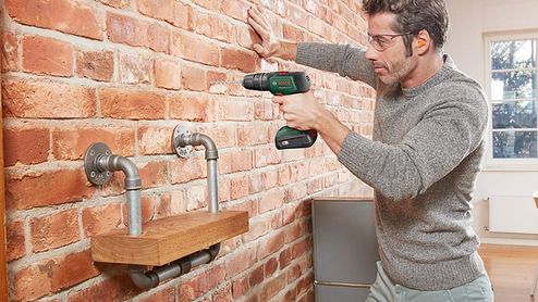 Hombre utilizando un taladro inalámbrico sobre una pared de ladrillo.