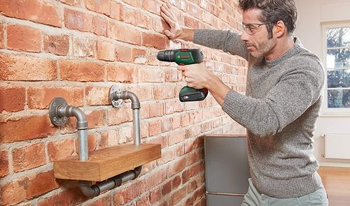 Hombre utilizando un taladro inalámbrico sobre una pared de ladrillo.
