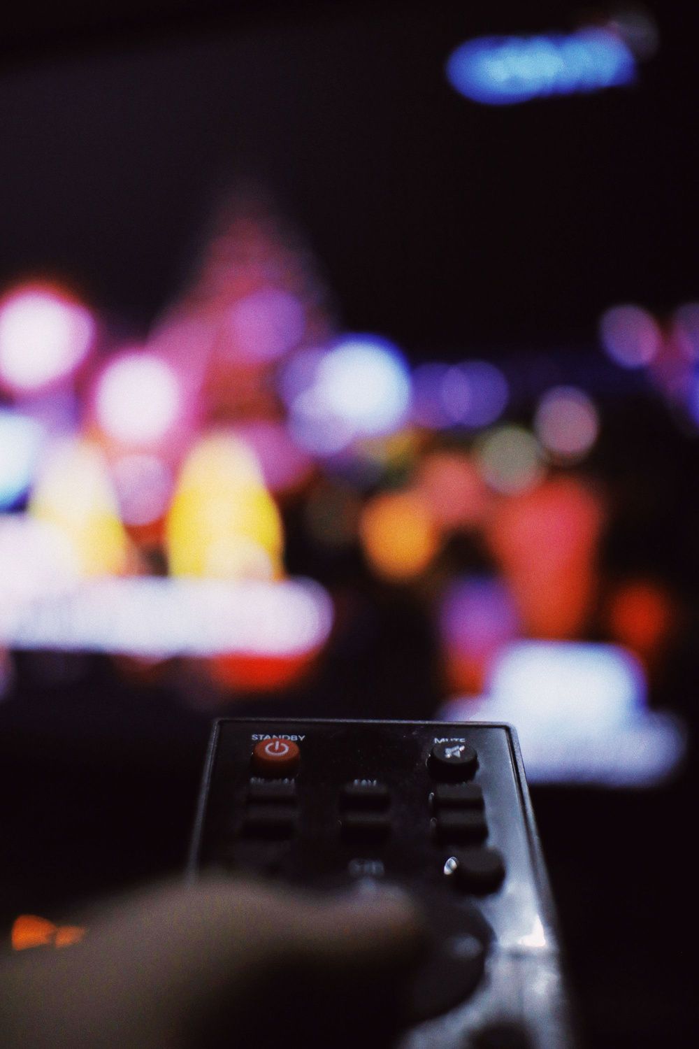 Mano sujetando un mando a distancia, con un televisor desenfocado al fondo.