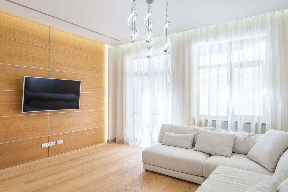 Televisor colgado en una pared de madera frente a un sofá blanco, en un salón luminoso.