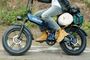 Primer plano de una bicicleta eléctrica UrLife T5 azul en marcha, con neumáticos anchos y equipaje en el portaequipajes trasero.