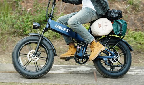 Primer plano de una bicicleta eléctrica UrLife T5 azul en marcha, con neumáticos anchos y equipaje en el portaequipajes trasero.