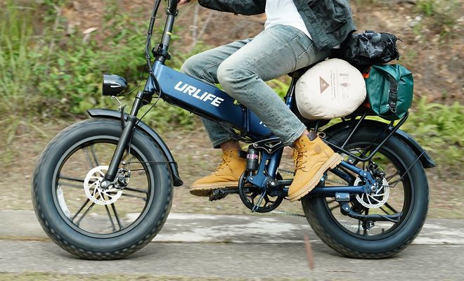 Primer plano de una bicicleta eléctrica UrLife T5 azul en marcha, con neumáticos anchos y equipaje en el portaequipajes trasero.