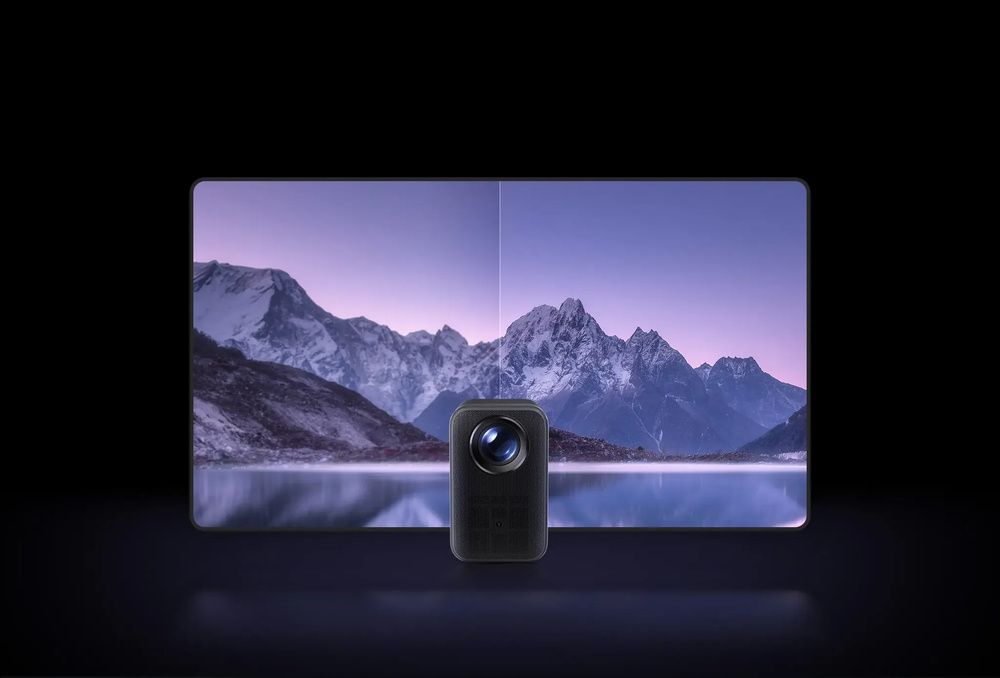 Proyector Xiaomi frente a una imagen de montañas reflejadas en un lago, proyectada sobre una pared.