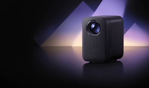 Proyector Xiaomi Smart Projector L1 Pro negro sobre una superficie reflectante, con iluminación violeta de fondo.