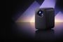 Proyector Xiaomi Smart Projector L1 Pro negro sobre una superficie reflectante, con iluminación violeta de fondo.