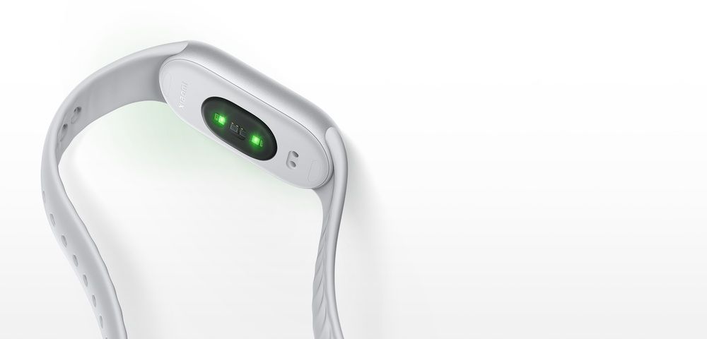 Vista trasera de una Xiaomi Smart Band 11 con correa clara y el sensor óptico iluminado en verde.