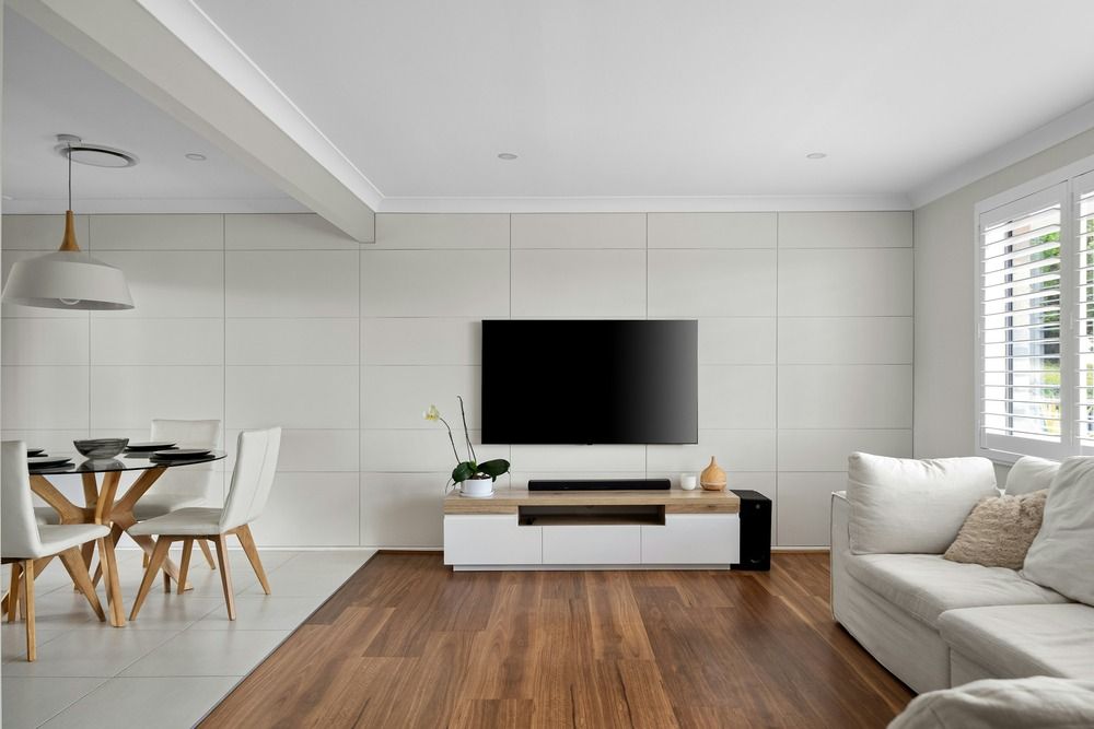 Smart TV montada en una pared blanca sobre un mueble de madera.